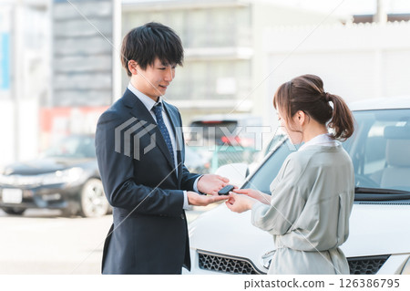 年輕銷售員將車鑰匙交給女顧客，男銷售員 126386795