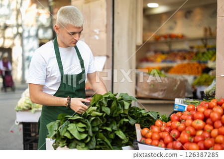 Guy shop seller puts spinach goods on display case 126387285