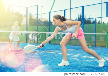 Woman actively playing paddle tennis on a court in a park against the background of glare 126387302