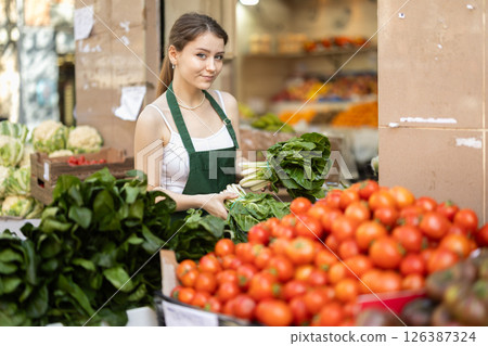 Young woman seller puts spinach in vegetable shop 126387324