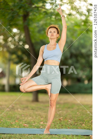 Focused female yoga practitioner performing Garudasana in garden 126387458