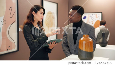 Woman, man and vase with tablet in art gallery for negotiation, discussion and explain deal. People, ceramics and customer with museum, guide and display with culture, talent or sculpture at event 126387500
