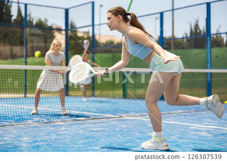 Young woman playing paddle tennis against team of women Young woman playing paddle tennis against team of women 126387539