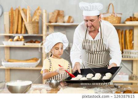 Daughter helps father baker to make pastries, lubricate croissants with loosened egg Daughter helps father baker to make pastries, lubricate croissants with loosened egg 126387615