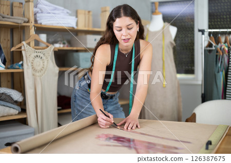 Woman tailor drawing on brown paper in workshop 126387675