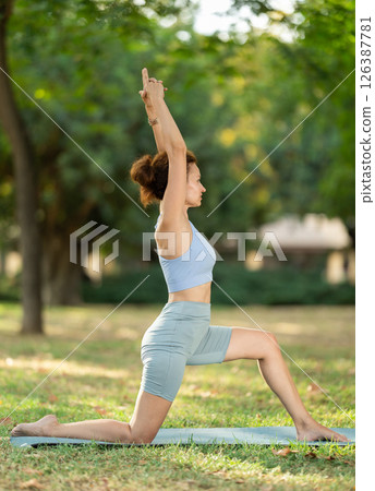 Slim woman practicing yoga - virabhadrasana pose in summer park Slim woman practicing yoga - virabhadrasana pose in summer park 126387781
