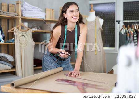 Woman tailor drawing on brown paper in workshop 126387828
