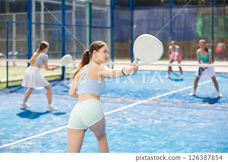 Young woman playing paddle tennis against team of women 126387854