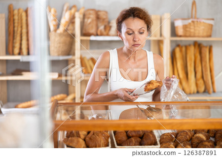 Woman packs croissant in plastic disposable bag in bakery shop 126387891