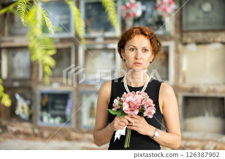 Drieving woman in black dress standing with bouquet by columbarium 126387902