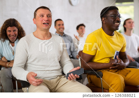 Smiling man listening to lecture in auditorium with male group Smiling man listening to lecture in auditorium with male group 126388021