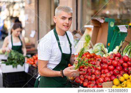 Portrait of young man seller with green onions in her hands - work in grocery supermarket Portrait of young man seller with green onions in her hands - work in grocery supermarket 126388093