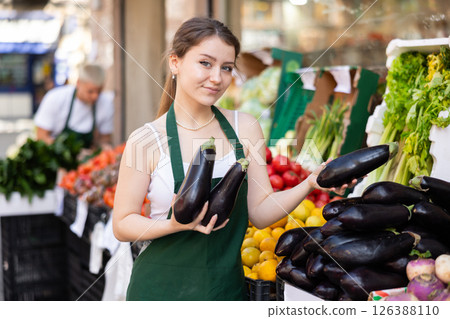 Young woman seller puts eggplants in vegetable shop Young woman seller puts eggplants in vegetable shop 126388110