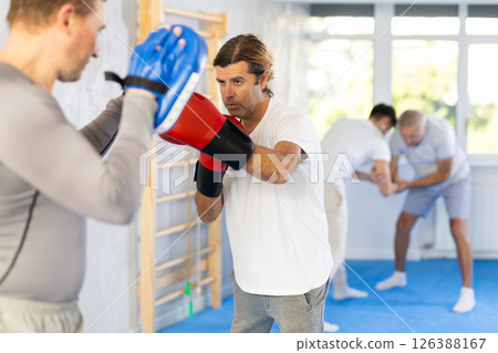 Man works out strength and speed of boxing punch mitts with help of partner in boxing paws 126388167