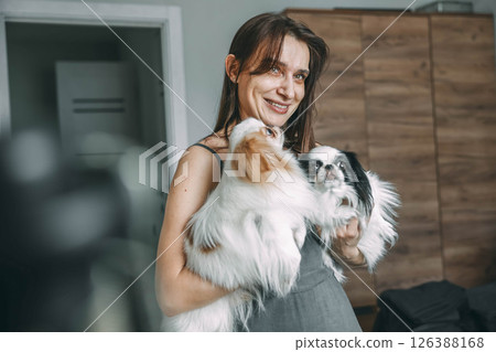 woman tenderly holding two japanese chin dogs, showcase affection and pet care at home 126388168