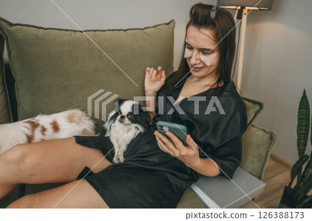 woman relaxing with smartphone during morning beauty routine with two japanese chin dogs at home woman relaxing with smartphone during morning beauty routine with two japanese chin dogs at home 126388173