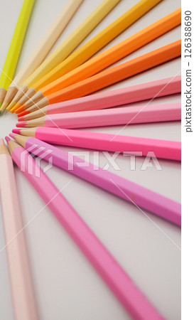 a spiral-like radial arrangement of warm-toned colored pencils, yellows, oranges, pinks, and purples, emanating outward in a fan shape. 126388690