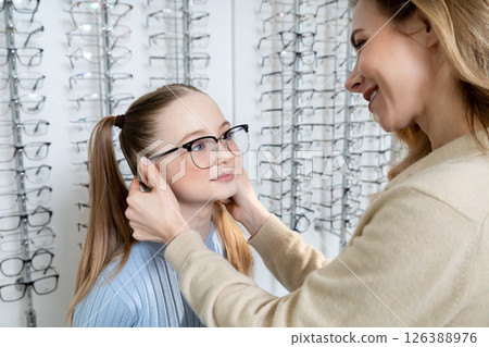 Mom and daughter in optic shop looking positive after choosing new eyeglasses Mom and daughter in optic shop looking positive after choosing new eyeglasses 126388976