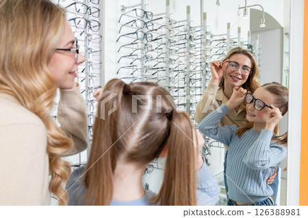 Mom choosing new eyeglasses for her cute little daughter in optic shop Mom choosing new eyeglasses for her cute little daughter in optic shop 126388981