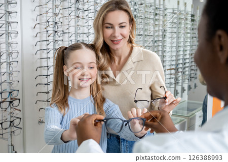 Mom and daughter choosing new eyeglasses in optic shop and looking interested Mom and daughter choosing new eyeglasses in optic shop and looking interested 126388993