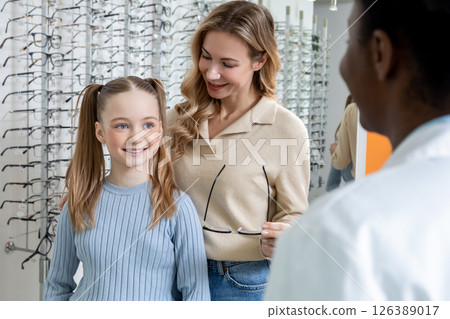 Mom and daughter choosing new eyeglasses in optic shop and looking interested 126389017