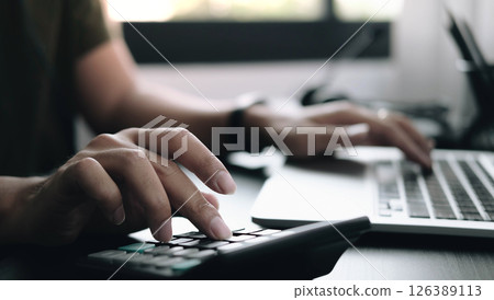 Close up Businessman using calculator and laptop for do math finance on wooden desk in office and business working background, tax, accounting, statistics and analytic research concept Close up Businessman using calculator and laptop for do math finance on wooden desk in office and business working background, tax, accounting, statistics and analytic research concept 126389113