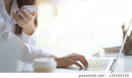 Cropped image of female holding smartphone getting message with confirmation making transaction on laptop computer,woman using mobile phone app for synchronizing data with netbook via bluetooth. Cropped image of female holding smartphone getting message with confirmation making transaction on laptop computer,woman using mobile phone app for synchronizing data with netbook via bluetooth. 126389168