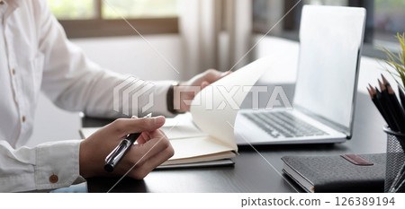 Closeup businessman writing on notebook on table with laptop. Closeup businessman writing on notebook on table with laptop. 126389194