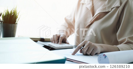 Close up Business woman using calculator and laptop for do math finance on wooden desk in office and business working background tax accounting statistics and analytic research concept 126389210