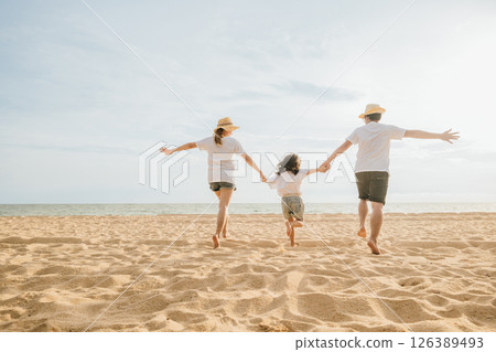 Happy Asian parents with their daughters enjoying playful at beach. Little girls with their mother and father holding hand of child running and pretending on sand. Positive family outdoor activity 126389493