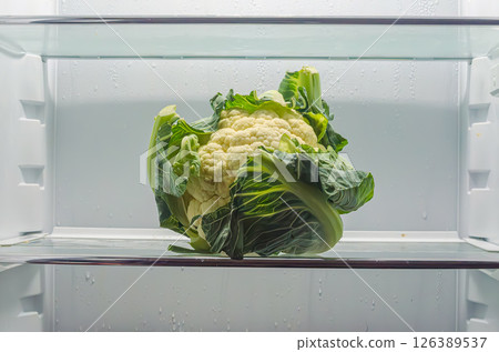 Cauliflower with vibrant green leaves placed on a shelf in a refrigerator. High quality photo Cauliflower with vibrant green leaves placed on a shelf in a refrigerator. High quality photo 126389537