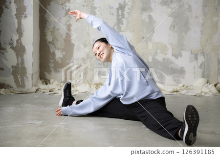 A woman warming up for dancing or sports stretches her arms and legs, bending forward with her legs apart 126391185