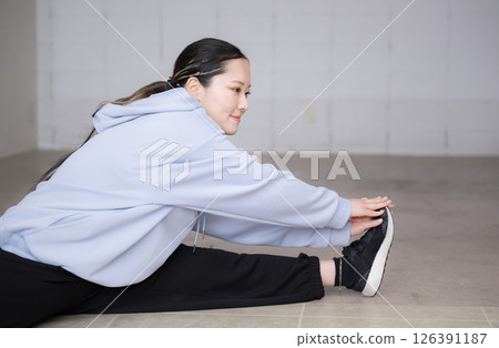 一位女士正在為舞蹈或運動熱身，伸展手臂和腿，雙腿分開向前彎曲 126391187