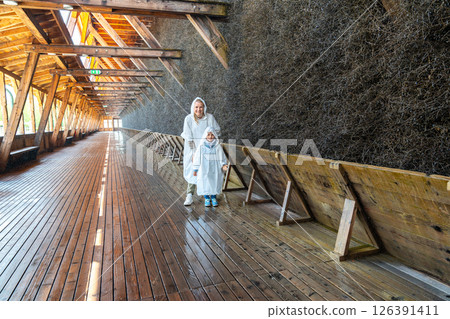 Two people wearing raincoats explore a wooden salt graduation tower. The structure's wooden beams and walls create an atmospheric scene, highlighting architectural details Two people wearing raincoats explore a wooden salt graduation tower. The structure's wooden beams and walls create an atmospheric scene, highlighting architectural details 126391411