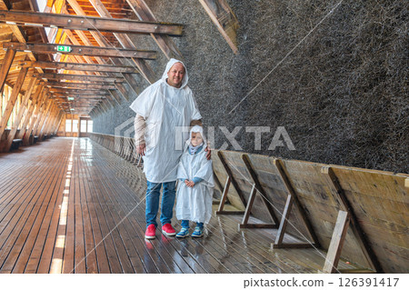 Father and child wearing protective capes in a traditional salt graduation tower. They are smiling and enjoying the experience, surrounded by the unique wooden structure. 126391417