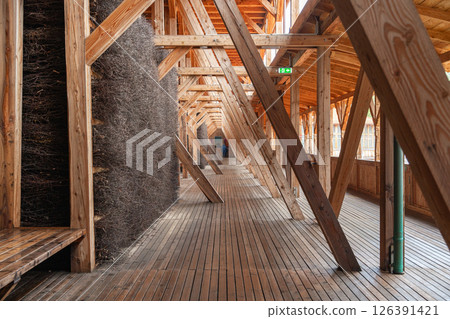 Wooden architectural interior with large beams and natural materials creating a unique passageway. A person stands in the background, adding scale to the geometric design. Salt Graduation Tower Wooden architectural interior with large beams and natural materials creating a unique passageway. A person stands in the background, adding scale to the geometric design. Salt Graduation Tower 126391421