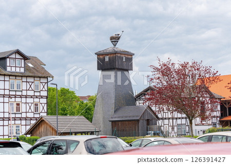 Stork nest perched atop a vintage timber-frame building tower amidst traditional houses and parked cars, capturing a harmonious blend of nature and architecture on a cloudy day. 126391427