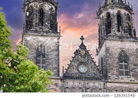 Magdeburg gothic medieval cathedral Dom historic facade church towers green tree dramatic warm purple sunset sky. Scenic Saxony-Anhalt sightseeing landmark detailed architecture central clock Germany Magdeburg gothic medieval cathedral Dom historic facade church towers green tree dramatic warm purple sunset sky. Scenic Saxony-Anhalt sightseeing landmark detailed architecture central clock Germany 126391548