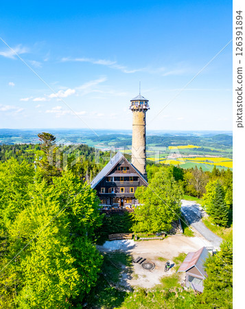 Aerial view captures Svatobor Lookout Tower surrounded by lush trees and hills in Czechia. The sunny day reveals vibrant colors of the landscape, inviting exploration and enjoyment. 126391894