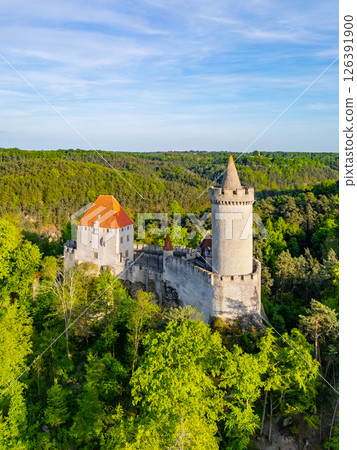 Kokorin Castle stands majestically amid lush greenery during a sunny evening. An aerial perspective showcases its historic architecture and the beauty of its natural surroundings. 126391900