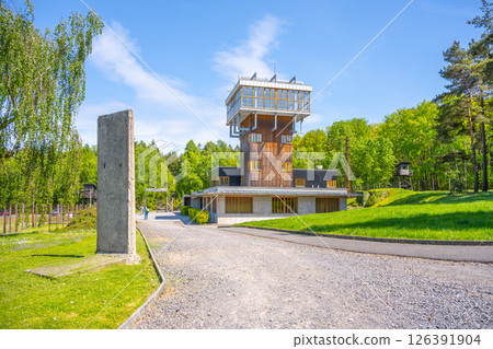 Visitors enjoy the serene surroundings of the former Vojna prison complex in Lesetice, Czechia, featuring a notable watch tower surrounded by lush greenery and modern structures. 126391904