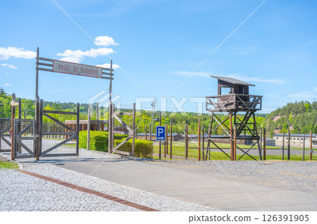 The entrance gate to the former Vojna prison complex in Lesetice, Czechia features a watchtower and surrounding fencing. This site stands as a historical landmark reflecting its past. 126391905