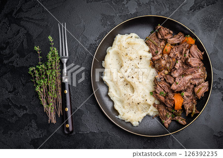 Beef stew with mashed potatoes, carrots and herbs on a plate isolated. black background. top view 126392235