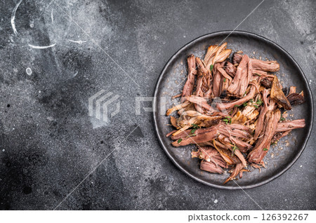 A tantalizing plate of pulled brisket, slow-cooked to perfection, drizzled with barbecue sauce for added flavor. black background. top view A tantalizing plate of pulled brisket, slow-cooked to perfection, drizzled with barbecue sauce for added flavor. black background. top view 126392267