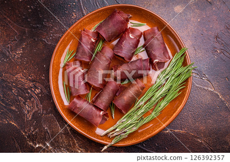 Typical dried spanish meat cecina, spanish beef jamon on plate with rosemary. brown background. top view Typical dried spanish meat cecina, spanish beef jamon on plate with rosemary. brown background. top view 126392357