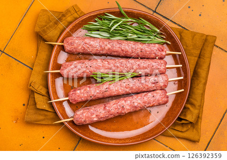 Raw Turkish Urfa kebab skewers on a plate with herbs. orange background. top view Raw Turkish Urfa kebab skewers on a plate with herbs. orange background. top view 126392359