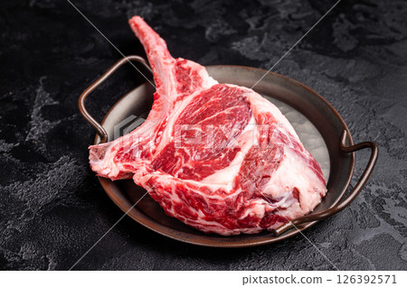 Raw tomahawk steak with marbling, fresh rib eye with bone. black background. top view Raw tomahawk steak with marbling, fresh rib eye with bone. black background. top view 126392571