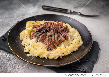 German Braised Beef Cheek, Slow cooked meat with smashed potatoes on a plate. grey background. top view 126392582