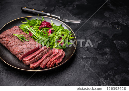 Grilled and sliced Flank beef steak on plate with salad. black background. top view 126392628