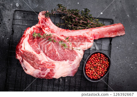 Uncooked tomahawk steak, raw black angus beef rib eye with bone. black background. top view Uncooked tomahawk steak, raw black angus beef rib eye with bone. black background. top view 126392667